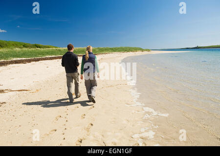 Junge Frau und Mann zu Fuß an einem schönen Sandstrand im Sommer Sonnenschein, Glims Holm, Orkney Inseln, Schottland. Stockfoto