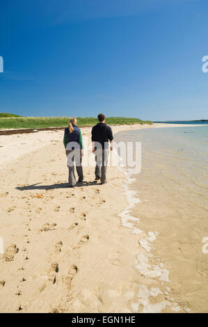 Junge Frau und Mann zu Fuß an einem schönen Sandstrand im Sommer Sonnenschein, Glims Holm, Orkney Inseln, Schottland. Stockfoto