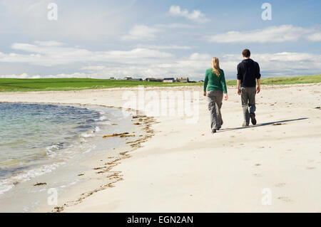 Junge Frau und Mann zu Fuß an einem schönen Sandstrand im Sommersonnenschein, Burray, Orkney Inseln, Schottland. Stockfoto