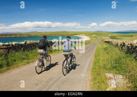 Junger Mann und Frau Radfahren entlang einer ruhigen Straße auf South Ronaldsay, Orkney Inseln, Schottland. Stockfoto