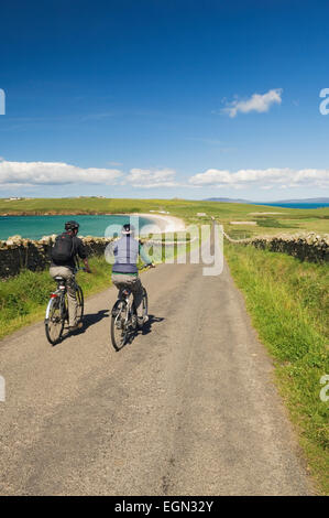 Junger Mann und Frau Radfahren entlang einer ruhigen Straße auf South Ronaldsay, Orkney Inseln, Schottland. Stockfoto