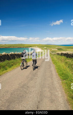 Junger Mann und Frau Radfahren entlang einer ruhigen Straße auf South Ronaldsay, Orkney Inseln, Schottland. Stockfoto