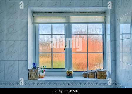 Milchglas Badezimmerfenster mit verzerrten außen Orange/blau und verschiedene Gegenstände auf der Fensterbank. Stockfoto