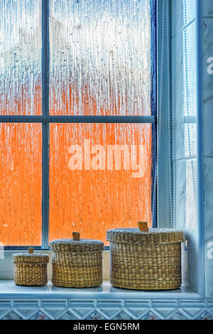 Satz von drei kleine Weidenkörbe sitzen auf einer Fensterbank Bad gegen eine mattierte Fenster mit verzerrt orange außen. Stockfoto