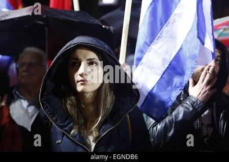 Athen, Griechenland. 27. Februar 2015. Eine junge Frau ist während der KKE-Protest vor einer griechischen Flagge abgebildet. Tausende von Griechen folgten dem Aufruf der kommunistischen Partei von Griechenlands (KKE) trotz starken Regens, um gegen die Politik der griechischen Regierung zu protestieren, die weiterhin der Sparpolitik zu folgen, wie von der Eurogruppe, trotz unterschiedlicher Wahlversprechen gefordert. Bildnachweis: Michael Debets/Alamy Live-Nachrichten Stockfoto
