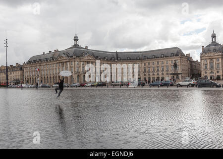 Mädchen mit ihrem Schirm in den Miroir d ' Eau in Place De La Bourse springen. Stockfoto