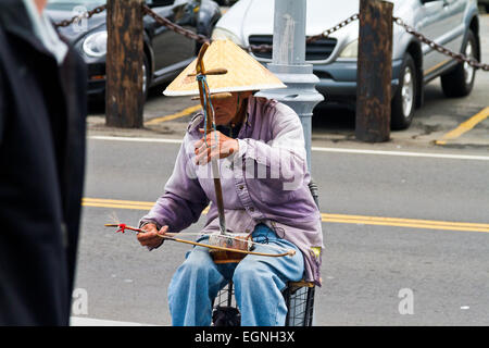 Ein älterer chinesischer Mann trägt einen traditionellen Hut und ein traditionelles Instrument zu spielen, auf der Straße in San Francisco. Stockfoto