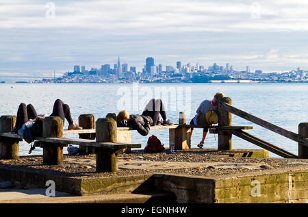 Eine Gruppe von jungen Menschen auf Bänken in Sausalito, Kalifornien mit der Skyline von San Francisco in der Ferne entspannen. Stockfoto