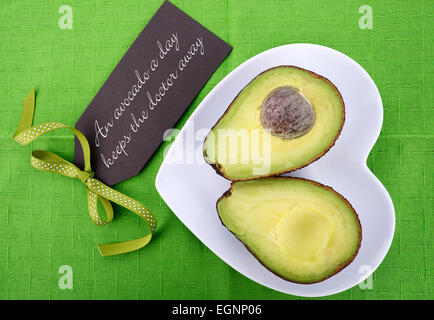 Avocado halbieren auf Herz Form Platte auf helle grüne Tischdecke mit Nachricht Gruß Tag schneiden. Stockfoto