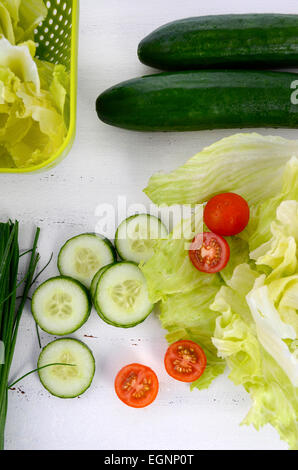 Zubereitung Salat mit Gurken, Salat, Cherry-Tomaten und Schnittlauch auf modernen weißen Holz Tisch setzen, overhead vertikale Ansicht Stockfoto