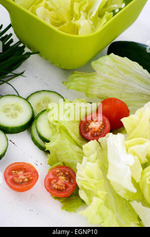 Zubereitung Salat mit Gurken, Salat, Cherry-Tomaten und Schnittlauch auf modernen weißen Holz Tischdekoration, Closeup vertikal. Stockfoto