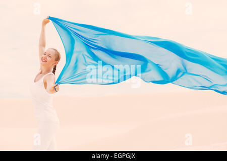 Junge schlanke Frau trägt weiß mit blauen Schal in Wüste fliegen Stockfoto