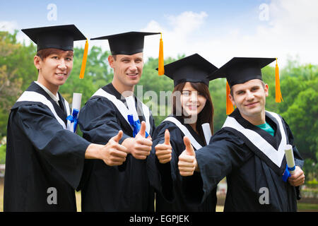 glückliche Schüler in Graduierung Kleider Diplome mit Daumen auftauchen Stockfoto