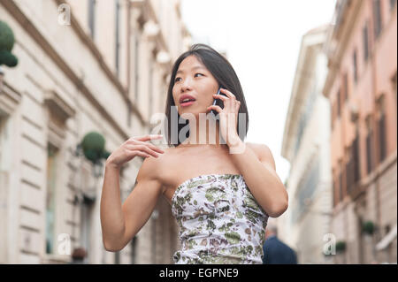 Junge schöne asiatische Frau schaut sich um und sprechen über Handy urban outdoor Frühjahr dressing Stockfoto