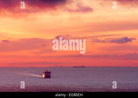 Dover. Die 'DFDS Seaways' Autofähre auf See fährt im Morgengrauen über den Ärmelkanal mit einem roten Himmel und Wolken am Horizont über der französischen Küste. Stockfoto