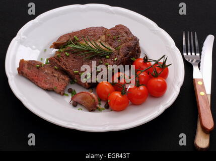 Rib-Eye Steak, Knoblauch, Kirschtomaten, Kräuter auf schwarzem Hintergrund, Ansicht von oben Stockfoto