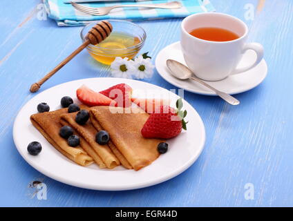 Stapel Pfannkuchen, frische Erdbeeren Heidelbeeren und Honig auf blau aus Holz Stockfoto