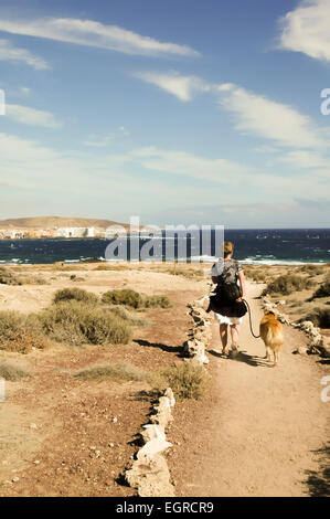 Frau, die ihren Hund in Richtung Meer auf dem Fußweg von Montaña Roja, El Medano, Teneriffa, Kanarische Inseln, Spanien Stockfoto