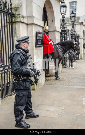 Bewaffneten Polizisten bewacht den zeremoniellen Guard zu Pferd an der beliebten Touristenstadt der Horse Guards in Whitehall, London, UK. Gun Sicherheit Stockfoto