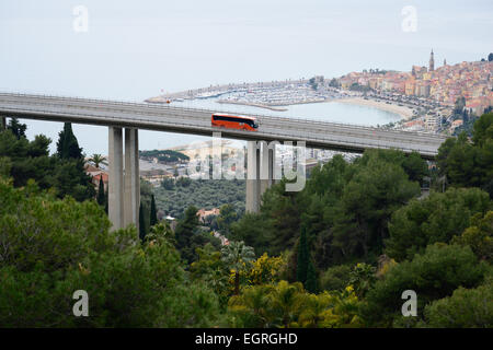 Sightseeing-Bus (mit Bewegungsunschärfen) auf einer Autobahnbrücke mit Blick auf die malerische Altstadt von Menton. Alpes-Maritimes, Französische Riviera, Frankreich. Stockfoto