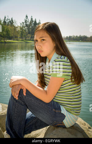 Vietnamesische/Kaukasische Mädchen sitzt meditierend 11-13 Jahr Jahre alt außerhalb Moody Stimmung Haltung Tween Tweens junger Mensch Menschen Natur natürliche Myrleen Pearson Stockfoto