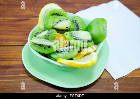 Teller mit in Scheiben geschnittenen Kiwis Zitronen und Orangen auf einem Holztisch Stockfoto