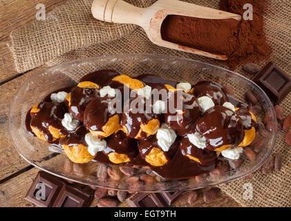 Schokolade Profitteroles mit Sahne, Kakaopulver, Kakaobohnen und Schokolade. Stockfoto