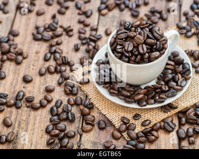 Weiße Espressotasse voll von gerösteten Kaffeebohnen auf einem rustikalen Holztisch. Horizontal / Querformat. Hintergrund. Stockfoto