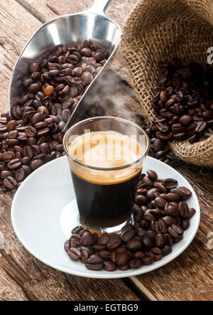 Espresso Kaffee in Glastasse mit Kaffeebohnen auf Holztisch. Stockfoto