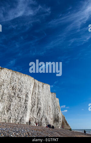 Tagesausflügler genießen die Wintersonne auf dem Kiesstrand unterhalb der ersten der sieben Schwestern Kreidefelsen im Cuckmere Haven. Stockfoto