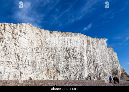 Tagesausflügler genießen die Wintersonne auf dem Kiesstrand unterhalb der ersten der sieben Schwestern Kreidefelsen im Cuckmere Haven. Stockfoto