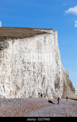 Tagesausflügler genießen die Wintersonne auf dem Kiesstrand unterhalb der ersten der sieben Schwestern Kreidefelsen im Cuckmere Haven. Stockfoto