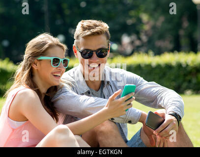 lächelnden Freunde mit Smartphones sitzen im park Stockfoto