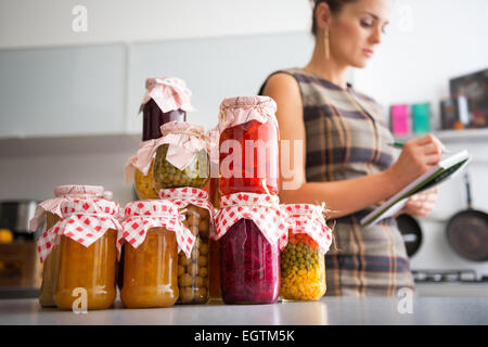 Closeup auf Gläser mit hausgemachte Früchte Marmelade, eingelegtes Gemüse und Hausfrau schreiben im Editor im Hintergrund Stockfoto