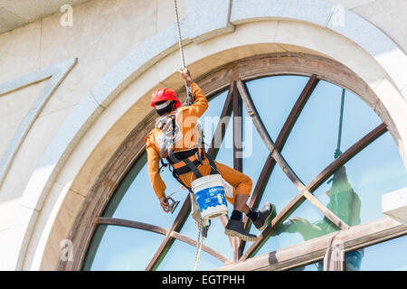 Fenster Reiniger tragen orange Overalls und roten Helm, unterbrochen von Gurtzeug und Seile Fensterputzen in Chennai, Indien Stockfoto