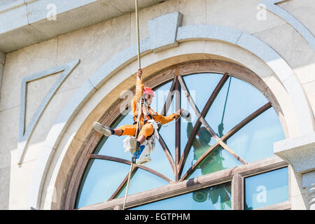 Fenster Reiniger tragen orange Overalls und roten Helm, unterbrochen von Gurtzeug und Seile Fensterputzen in Chennai, Indien Stockfoto