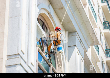 Fenster Reiniger tragen orange Overalls und roten Helm, unterbrochen von Gurtzeug und Seile Fensterputzen in Chennai, Indien Stockfoto