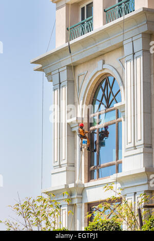 Fenster Reiniger tragen orange Overalls und roten Helm, unterbrochen von Gurtzeug und Seile Fensterputzen in Chennai, Indien Stockfoto