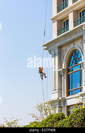 Fenster Reiniger tragen orange Overalls und roten Helm, unterbrochen von Gurtzeug und Seile Fensterputzen in Chennai, Indien Stockfoto