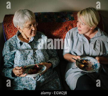Jüngere Frau und senior Frau essen Kuchen zusammen auf Sofa. Stockfoto
