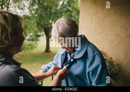 Jüngere Frau hilft senior Frau Knopf ihrer Jacke. Stockfoto