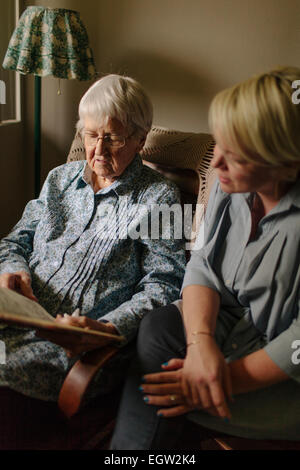 Ältere Frau im blauen Hemd auf Stuhl, mit jüngeren Frau neben ihr sitzt. Stockfoto