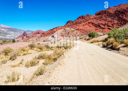 Unbefestigte Straße führt durch eine Wüste mit einer atemberaubenden roten Felsen-Hügel im Hintergrund in der Nähe von Tupiza, Bolivien Stockfoto