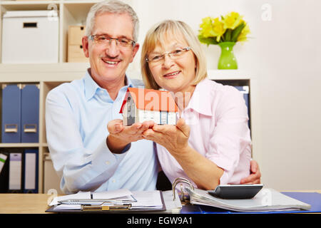 Alten lächelnden älteres Paar, ein kleines Haus in ihren Händen halten Stockfoto
