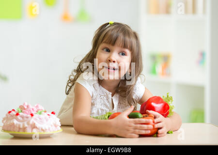 Kind gesundes Gemüse anstelle von süßen Kuchen auswählen Stockfoto