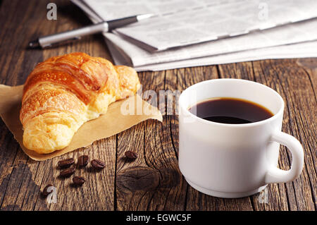 Tasse Kaffee, Croissant und Zeitung auf Holztisch Stockfoto