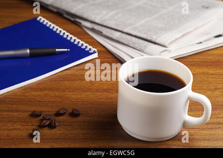 Tasse Kaffee, Zeitung und Notizblock auf Holztisch Stockfoto