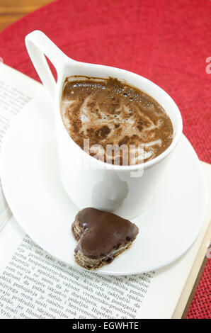Tasse Kaffee und Schokolade in Herzform auf ein Buch Stockfoto