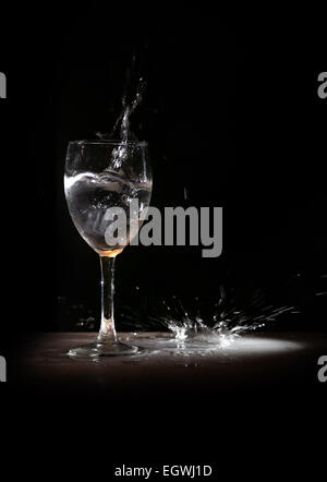 Glas Wein explodiert Wasser im Rampenlicht, spritzt eine Pfütze Stockfoto