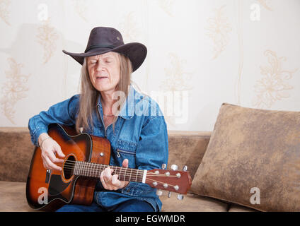 im mittleren Alter Mann mit Hut spielt Gitarre und singt zu Hause Stockfoto